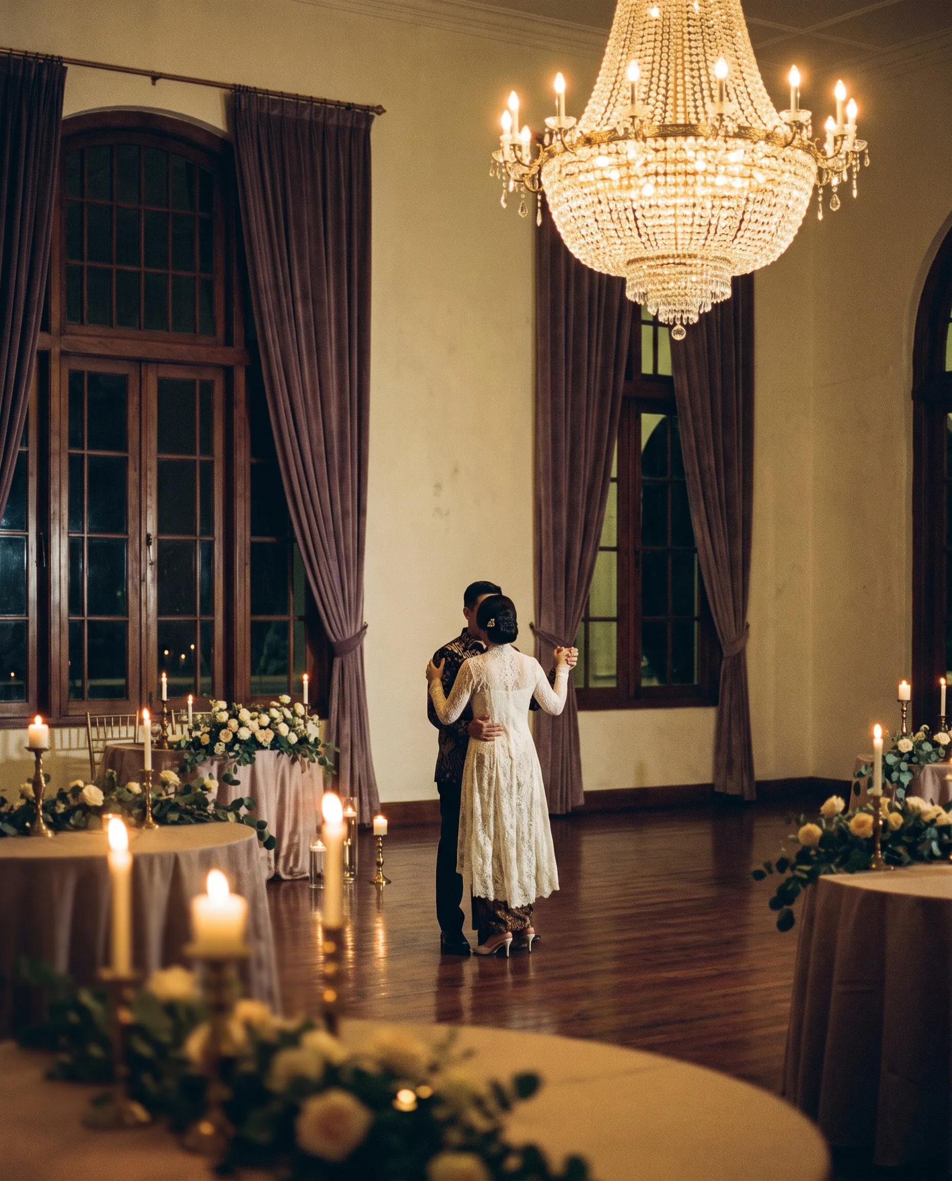 Sepasang pengantin berdansa berdua di bawah lampu kristal pada malam hari